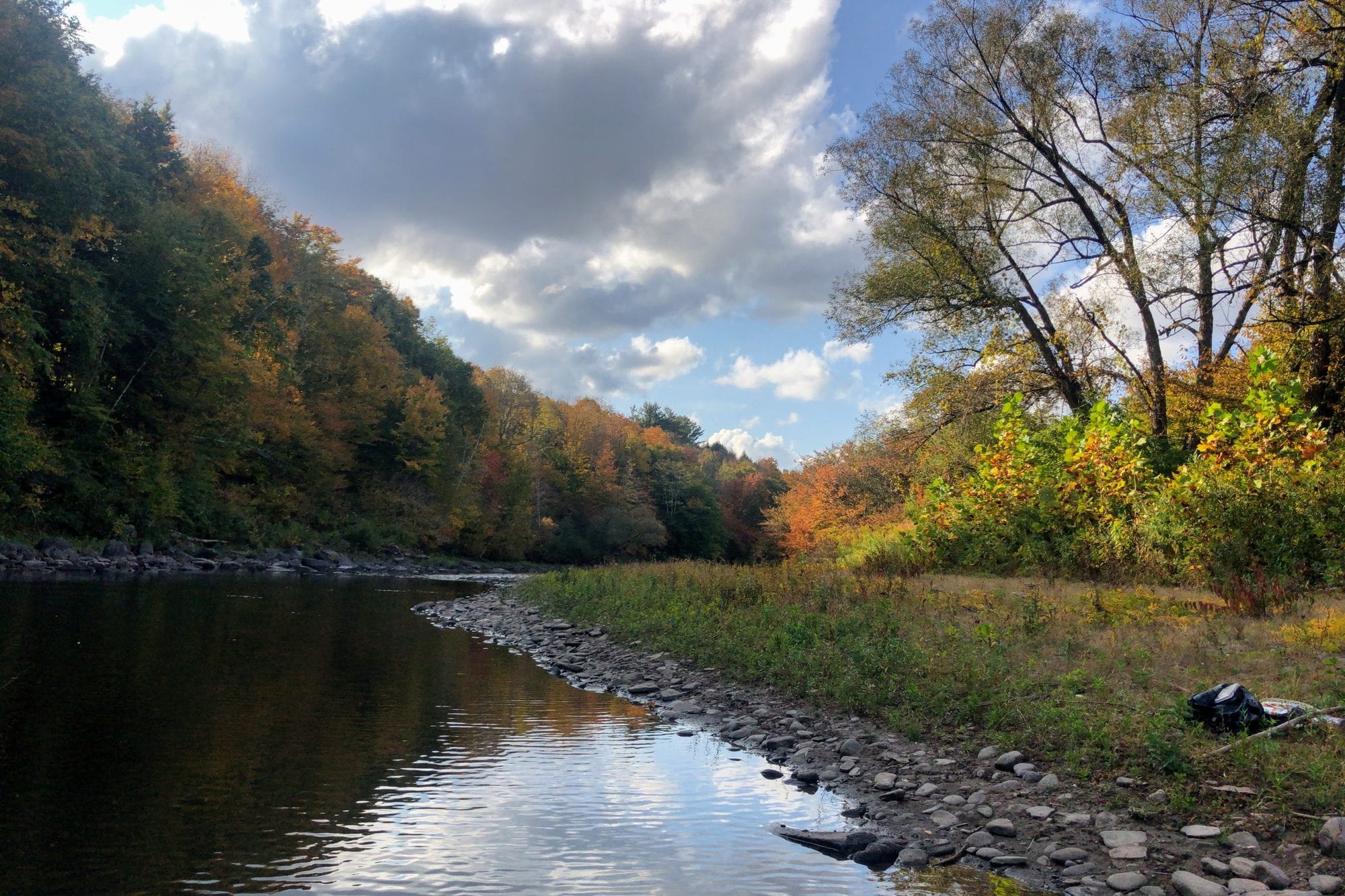 An autumn river beneath wooded hills and a cloudy sky